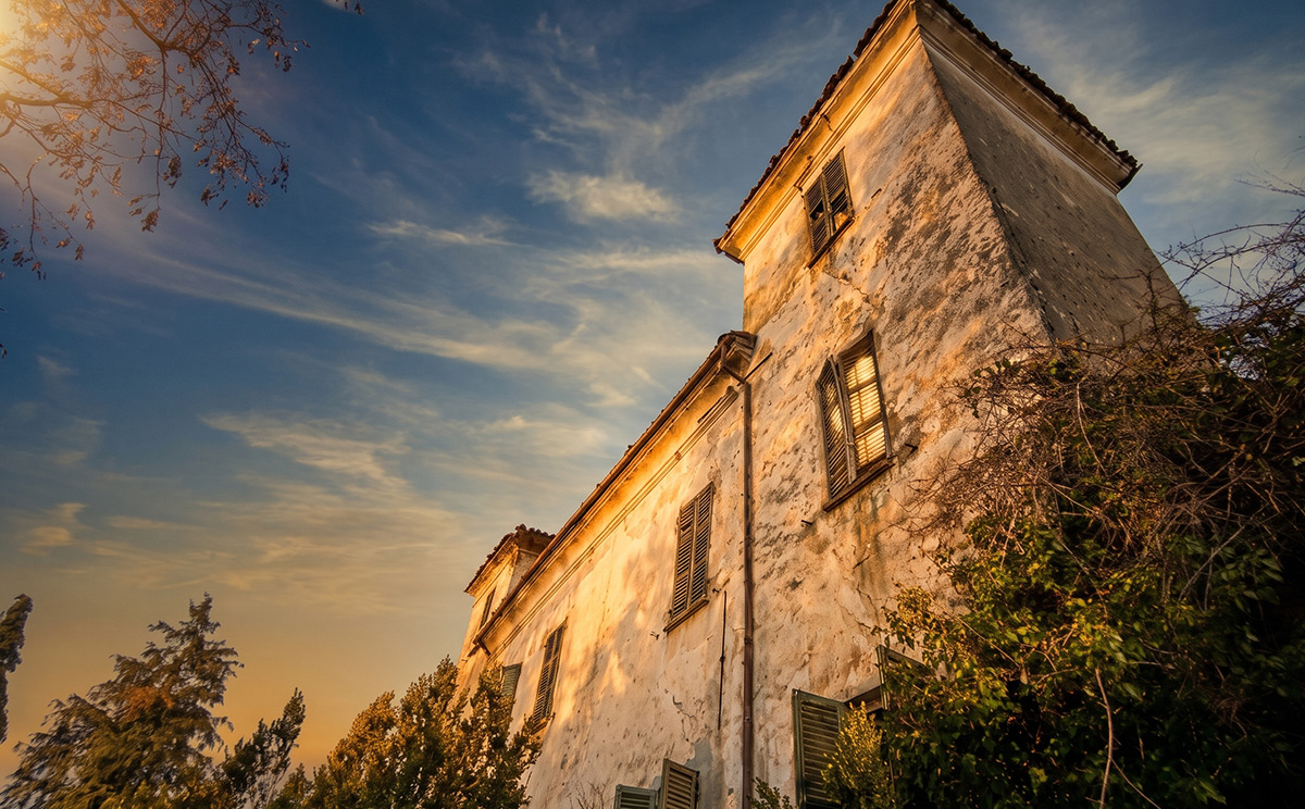 Weathered old house in Piedmont, Italy, with peeling plaster and shuttered windows glowing in the evening sun